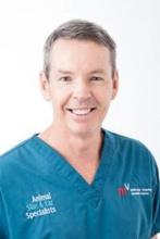 Dr Greg Burton smiles to camera in his blue scrubs