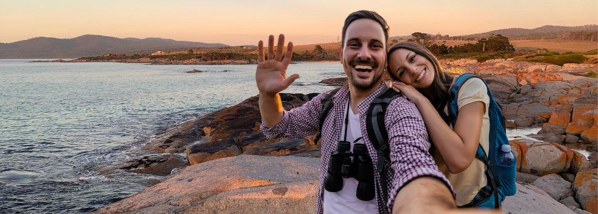 A man and woman smile to camera with a scenic view in the background