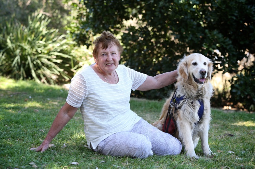 Woman and Golden Retriever sit outdoors on grass facing the camera